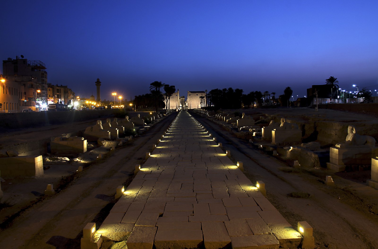 Illuminated Avenue of Sphinxes leading toward Luxor Temple beneath a deep blue evening sky